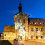 Bereits im frühen 11. Jahrhundert führte hier eine Brücke über den Fluss. Das in der Mitte des 14. Jahrhunderts gebaute Rathaus wurde nach einer Brandkatastrophe 1440 von den Bamberger Bürgern neu errichtet. Michael Küchel gestaltete es 1744-1756 im Stil des Barock und Rokoko um. Neben der wundervollen Architektur bestechen besonders die Fresken durch ihre Plastizität.