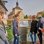 Eine Stadtführungsgruppe steht auf dem Ochsenklaviersteg an einer Tafel des Flusspfades entlang der Regnitz. Im Hintergurnd ist das Alte Rathaus.