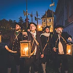 Eine Gruppe von Nachtwächtern steht bei Nacht mit ihren Leuchten und Hellebarden in der Altstadt Bambergs