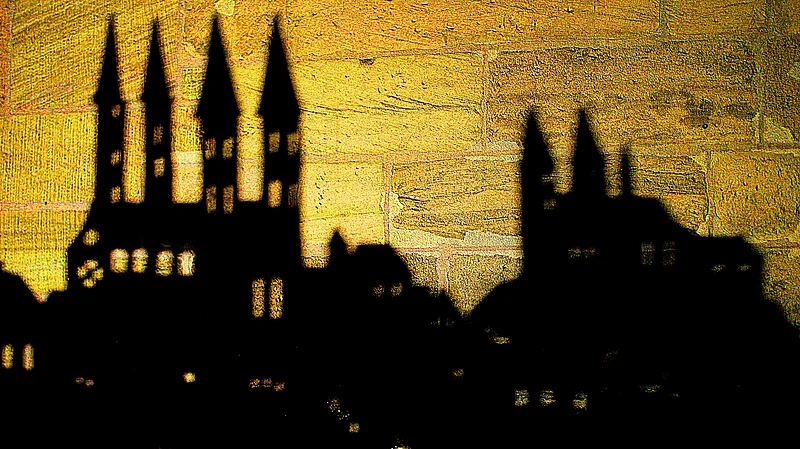 Eine Szene im Schattentheater in Bamberg. Die Konturen des Doms sind als Schatten auf die Sandsteinmauer der Katharinenkapelle geworfen.